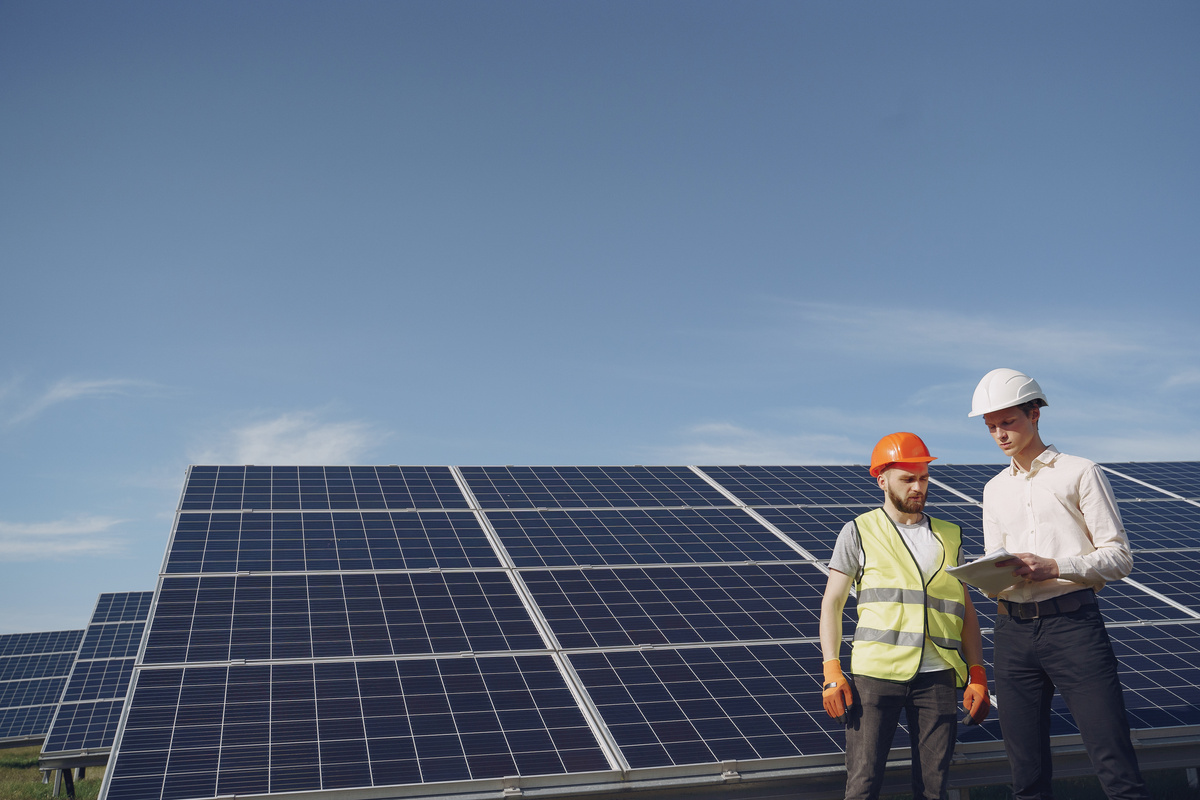 Two individuals in hard hats standing in front of solar panels